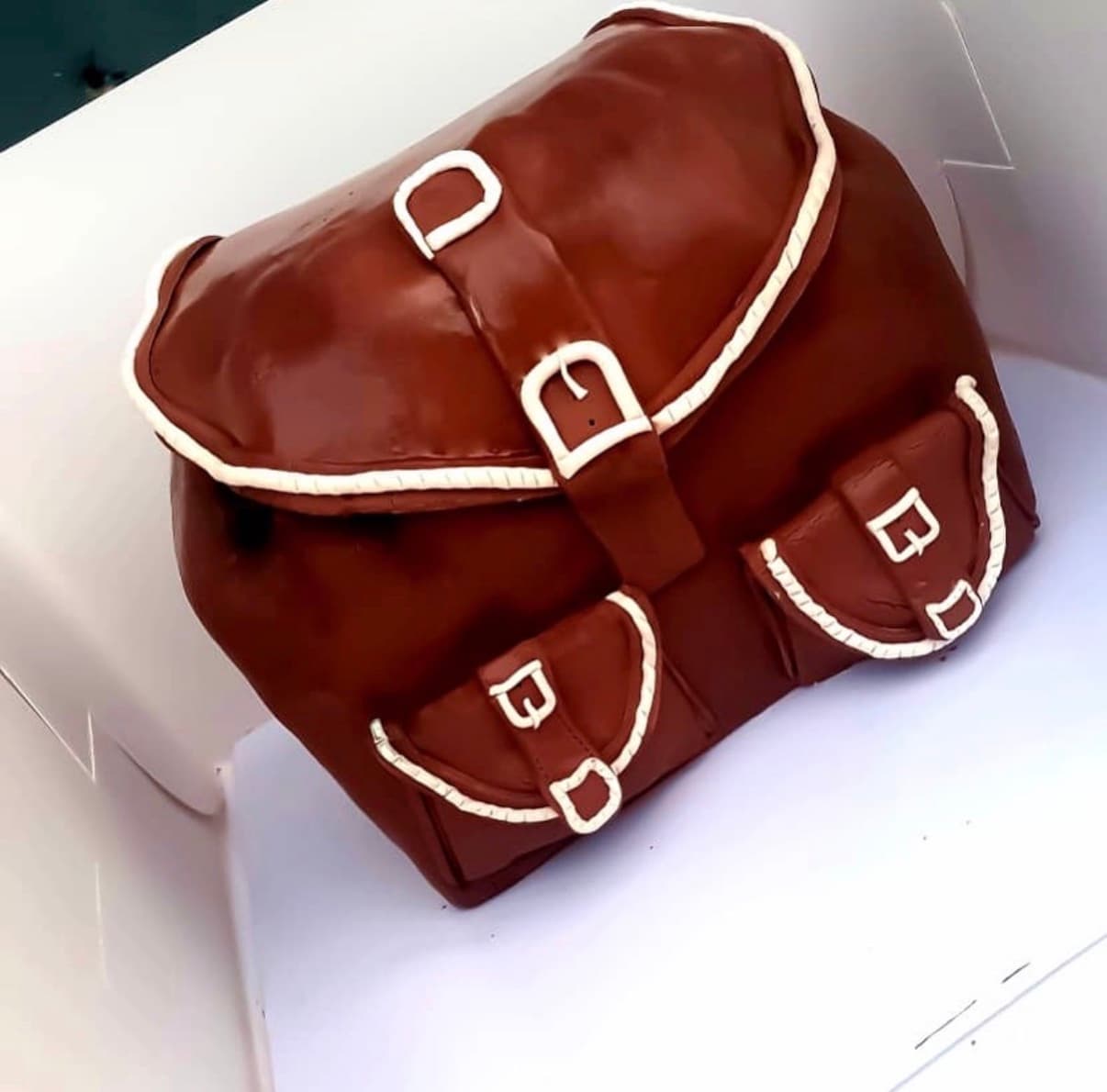 Sculpted brown satchel-shaped cake with buckles, pockets, piping, and handcrafted detailing