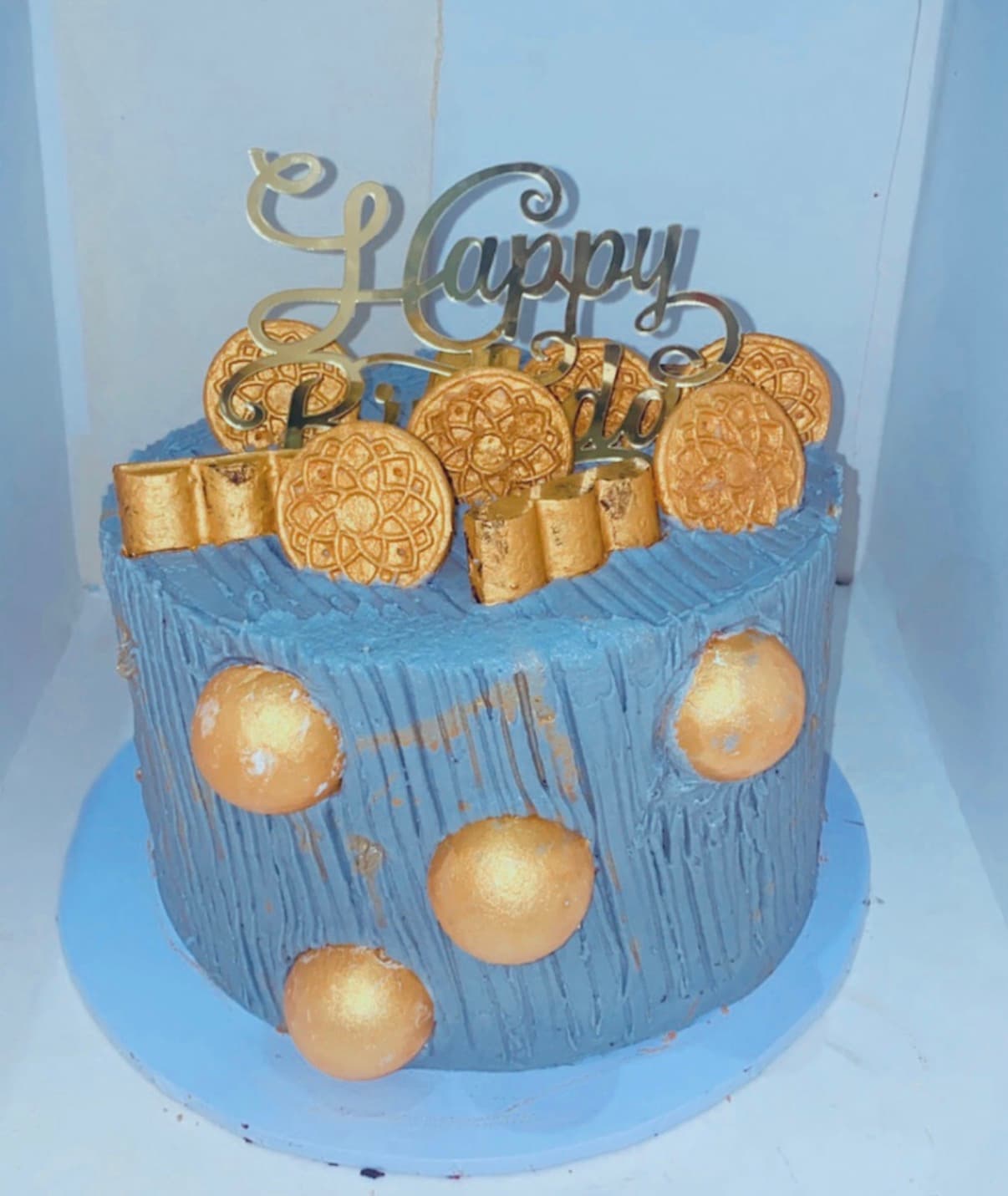 Deep-blue celebration cake decorated with metallic-gold accents, medallions, and a statement topper